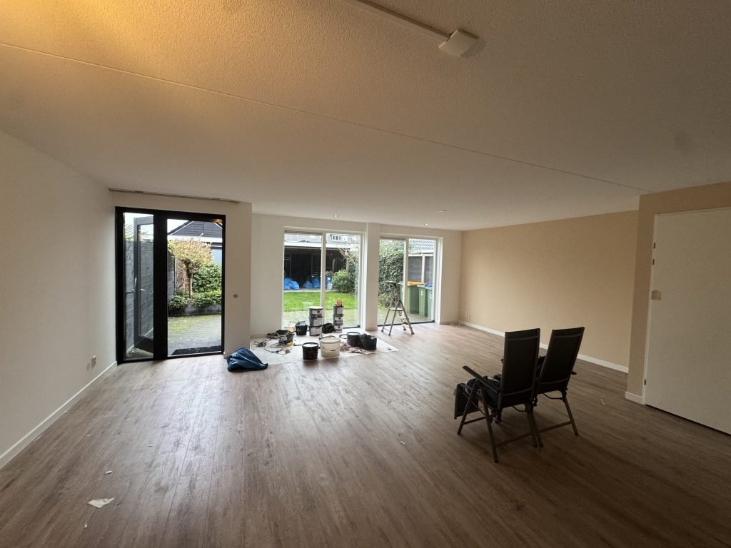 Leeggeruimde woonkamer van een bestaande woning met tuindeuren, verfemmers en een trapje op de vloer
